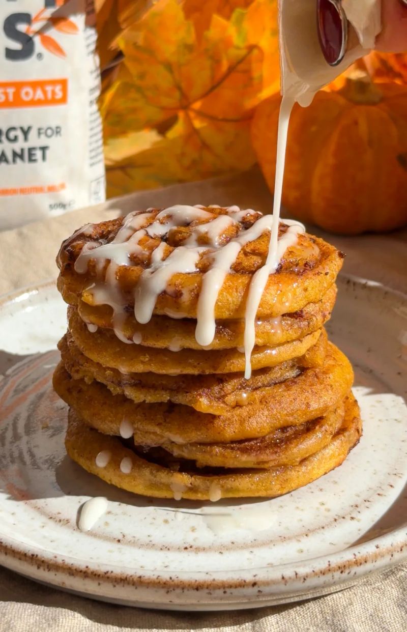 Pumpkin cinnamon roll pancakes with icing being poured ontop.
